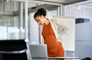 Black pregnant business woman suffering backache at modern office