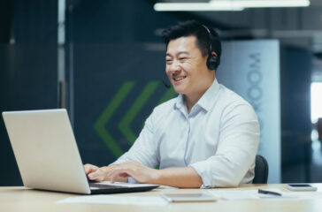 Portrait of a smiling young Asian man working in the office at a laptop in a headset