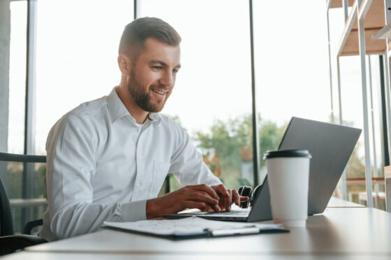Using laptop. Man in formal clothes is working in the modern office
